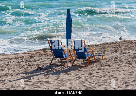 Pair of sun loungers and a folded beach umbrella on a deserted beach Stock Photo