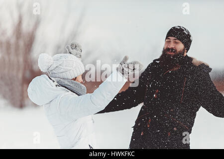 Girl in a white winter jacket, hat and mittens throws snow in the face of a man They have a great time on the winter holidays Stock Photo