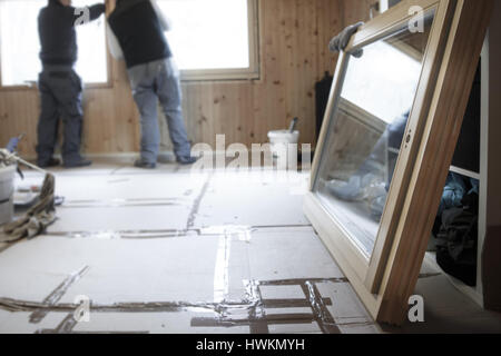 Workers in the background installing new, three pane wooden windows in an old wooden house, with a new window in the foreground. Home renovation, sust Stock Photo
