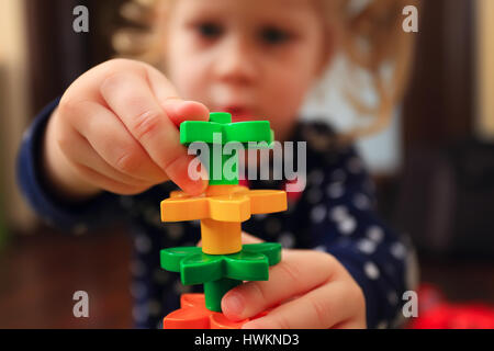 Child trying build tower with constructor close-up. Closeup of colorful constructor in kid hands.Tower of constructor on defocused child face backgrou Stock Photo