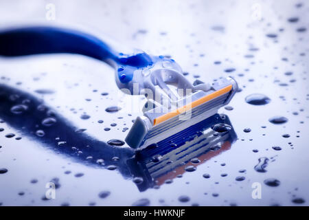 Wet disposable razor on blue background with water drops Stock Photo