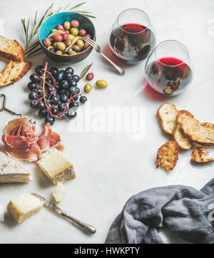 Wine and snack set. Variety of cheese, olives in ceramic bowl, prosciutto, roasted baguette slices, black grapes and glasses of red wine over grey mar Stock Photo
