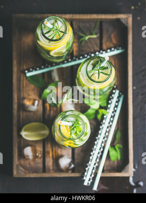 Citrus and herbs infused sassi water for detox, healthy eating, dieting in glass bottles in wooden tray over dark background, selective focus, top vie Stock Photo