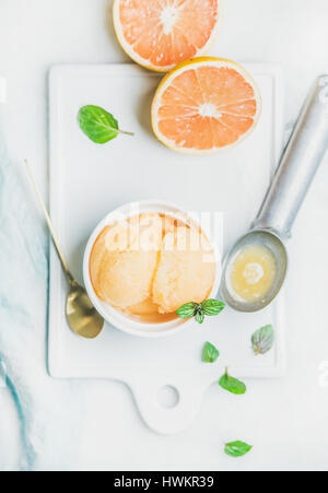 Pink grapefruit homemade sorbet with fresh mint leaves in white bowl on white board over light grey background, top view. Fresh healthy raw vegan summ Stock Photo