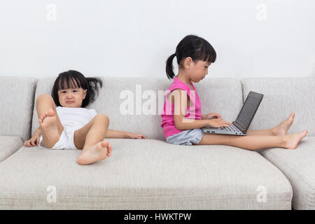 Asian Chinese little sisters fighting over a laptop on the sofa in the living room at home. Stock Photo