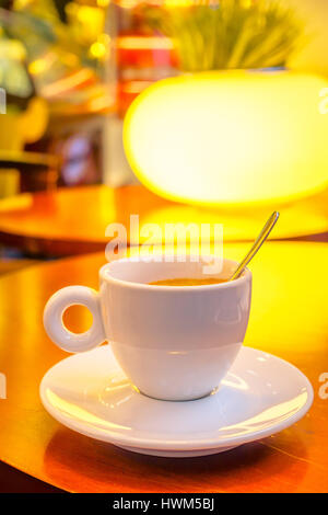 SHANGHAI, CHINA: Small white espresso cup sitting on saucer with coffee inside, cafeteria environment Stock Photo