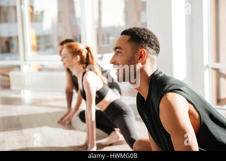 Cheerful african american young man doing yoga in group in studio Stock Photo