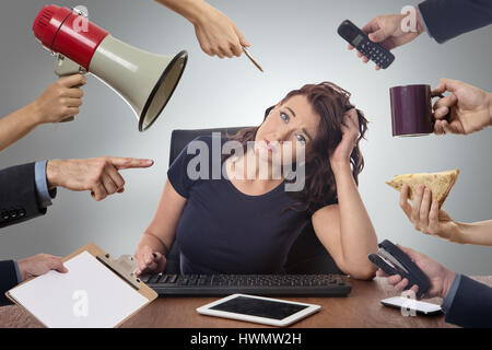 business woman sitting at desk surrounded by many hands holding objects Stock Photo