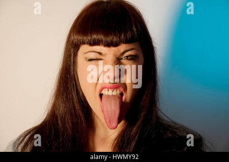 Young woman wearing piercings winking and sticking her tongue out Stock Photo