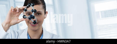 Portrait of female scientist holding molecular model against digital composite image of glass window Stock Photo