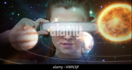 Close up of brunette wearing virtual reality simulator against composite image of solar system against white background 3d Stock Photo