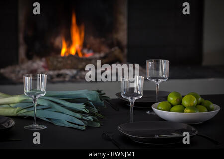 A laid out contemporary table - made out of a charred wood according to the shou-sugi- ban technique - in front of a fire in a modern interior. Stock Photo