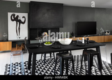 A laid out contemporary table - made out of a charred wood (shou-sugi-ban technique) - in a modern interior with fireplace. Lounge dining room. Stock Photo