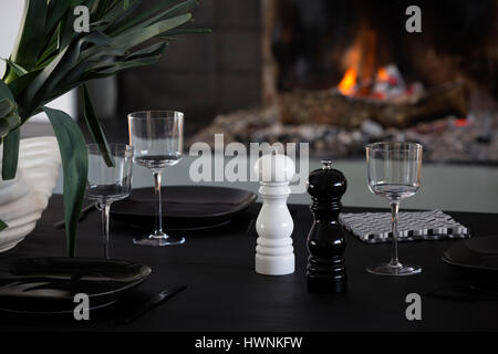 A laid out contemporary table - made out of a charred wood according to the shou-sugi- ban technique - in front of a fire in a modern interior. Stock Photo
