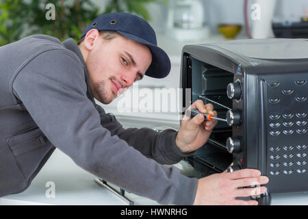 young repairman repairing oven with screwdriver in clients kitchen Stock Photo