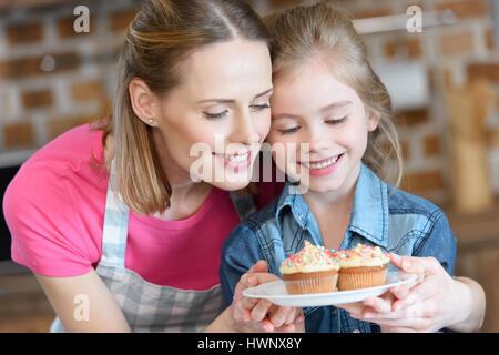 portrait of smiling mother and daughter holding plate with cupcakes Stock Photo