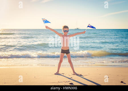 Cute smiling boy standing on the beach and holding Australian flags on Australia day Stock Photo