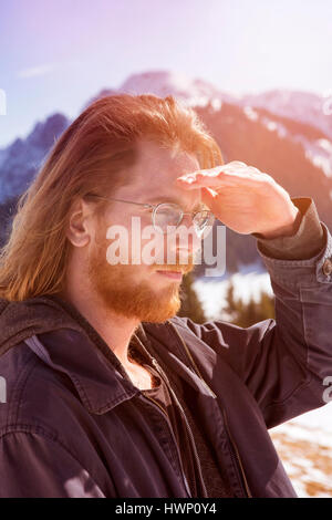 young red-haired bearded man surrounded by mountains looking into the distance