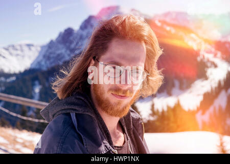 portrait of young red-haired bearded man surrounded by mountains