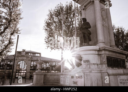 Lens flare illuminates 'Our Comrades have died for France' World War One memorial statue of soldier with market hall in background on side of CAnal de Stock Photo