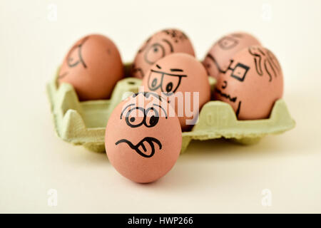 a pile of brown eggs ornamented with funny faces in a yellow egg carton, on an off-white background Stock Photo