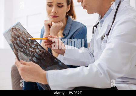 How could that happen. Worried patient focused woman looking concerned while her therapist explain her diagnosis and pointing at x-ray Stock Photo