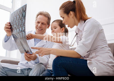 Let us check it together. Wise competent prominent surgeons looking through a brain scan and learning some new things together while girl paying a reg Stock Photo