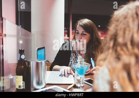 Two young beautiful caucasian women sitting in a bar using computer and smart phone hand hold, discussing - technology, business, studying concept Stock Photo