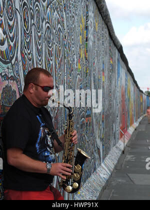 Berlin, Germany - 2013 July 30: Lone Saxophone player leaned against remnants of the Berlin Wall called East Side Gallery Stock Photo