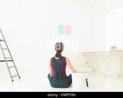 Rear view of a woman seating on a white floor choosing colour for painting a room against white background Stock Photo