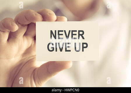 Closeup on businessman holding a card with text NEVER GIVE UP, business concept image with soft focus background and vintage tone Stock Photo