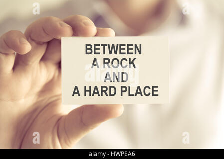 Closeup on businessman holding a card with text BETWEEN A ROCK AND A HARD PLACE, business concept image with soft focus background and vintage tone Stock Photo