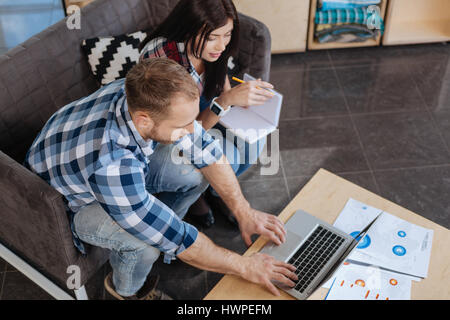 Modern workplace. Hardworking handsome young man pressing button and using a touchpad while showing something to his colleague Stock Photo