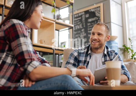 Being colleagues. Nice delighted young people sitting opposite each other and speaking to each other while discussing their work Stock Photo