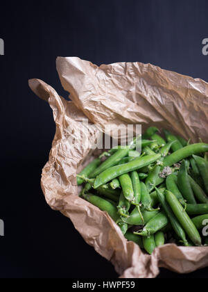 Fresh green peas in brown paper bag isolated on black background Stock Photo