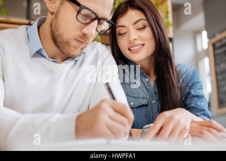 Pleasant teamwork. Cheerful positive nice colleagues sitting together and working on a project while being in the office Stock Photo