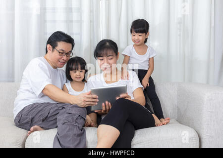 Happy Asian Chinese family using tablet on the couch in the living room at home. Stock Photo