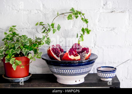 Close-up of pomegranate in plate on bowl by potted plant on table against brick wall Stock Photo