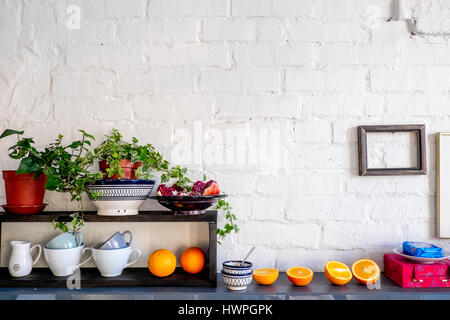 Potted plants and fruits with kitchen utensils on table against brick wall Stock Photo