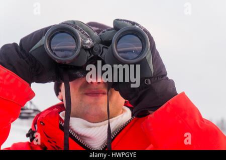 Close-up of man looking through binoculars while standing on snow covered field Stock Photo
