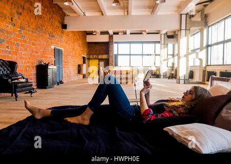 Full length side view of young woman using tablet computer while lying on bed at home Stock Photo