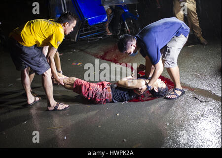 October 5, 2016 - Manila, National Capital Region, Philippines - Plain clothes policemen move the lifeless body of drug suspect Benjamin Visda on a muddy unpaved road 100m from Tondo Police Station 1. Police at the scene claimed that Visda, who was handcuffed, had resisted arrest and was killed in a struggle after he had grabbed one of the officers' guns. Eyewitnesses at the scene who refused to be identified claimed that Visda was beaten by ununiformed police as he pleaded for his life before being shot in the back of the head. The claimed that the policemen then removed his handcuffs, which  Stock Photo