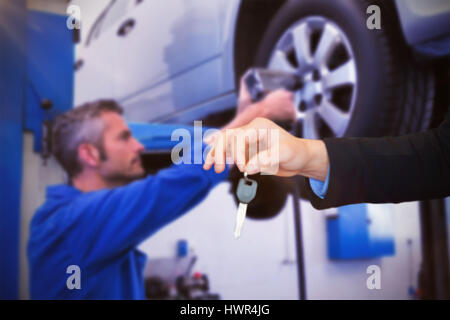 Customer receiving car keys against mechanic adjusting the tire wheel Stock Photo