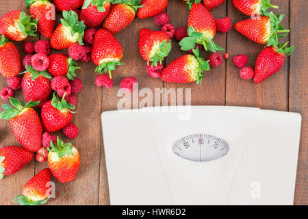 weighting scale against fresh strawberries and raspberries on wooden board Stock Photo