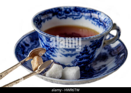 Antique blue and white china cup and saucer of black English breakfast tea with silver tongs for white and brown sugar cubes. Isolated on white backgr Stock Photo