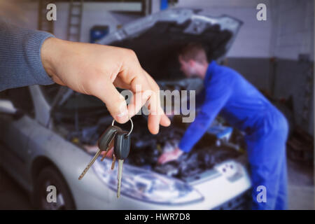 Smiling woman receiving keys from somebody against mechanic examining car engine Stock Photo
