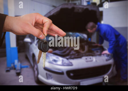 Happy woman receiving car keys against mechanic examining car engine Stock Photo