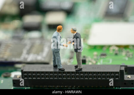 business agreement by two mini businessman shake hand on mainboard background - can use to display or montage on product Stock Photo