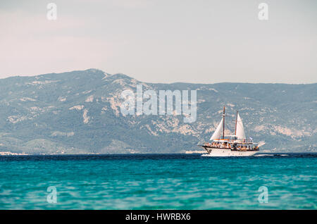PEFKOHORI, GREECE - MAY 26, 2015: Sailing ship sails in the Aegean Sea on the background of mountains and hills of the peninsula Sithonia, Halkidiki. Stock Photo