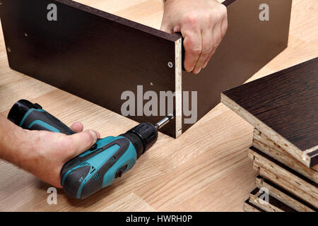 Assembling furniture from chipboard, using a cordless screwdriver, close up. Stock Photo
